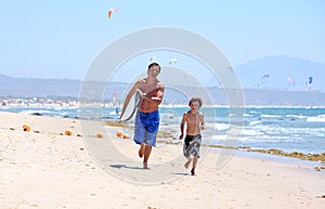 Young father and son running along beach with surfboard