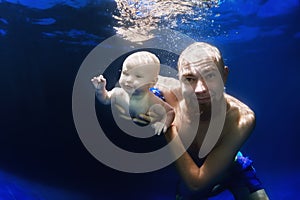 Young father swimming underwater with baby son in the blue pool