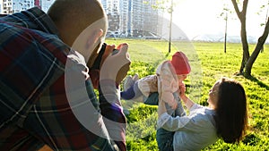 Young father taking pictures of mother and daughter playing in the park at sunset. Happy family photographed in nature