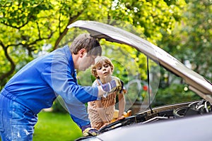 Young father teaching his little son to change motor oil in family car