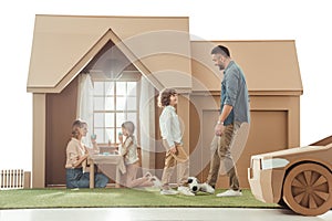 young father teaching his som to play soccer on yard of cardboard house