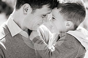 A young father with a three-year-old son are hugging and smiling outdoors, black and white. The concept of raising a happy child