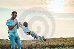 A young father throws his young son in the evening sunshine. Father`s Day. Father holding his little son, spinning him. Autumn