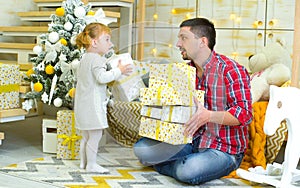 Young father and toddler daughter holding gift boxes near decorated Christmas tree at home