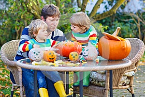 Young father and two little sons making jack-o-lantern for halloween in autumn garden