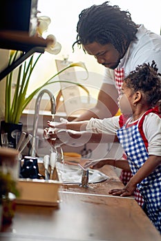 Young father washing dishes with her little daughter in a domestic kitchen, working as a team