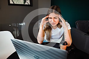 Young fatigued woman working at office desk in front of laptop, suffering from chronic daily headaches