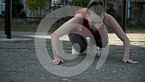 young female in activewear sitting, holding hands on ground in plank position