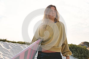 Young Female Adventurer At The Beach Walking Down Sand Dunes With Surf Board Or Kite Surfing Sunset