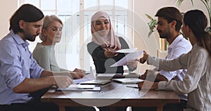 Young female arabian leader giving out paper documents to colleagues.