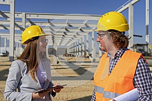 Young Female Architect with Digital Tablet and Engineer Having Conversation at Construction Site