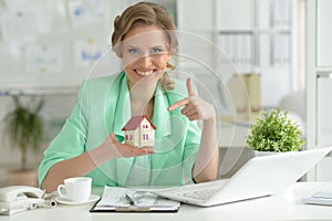 Portrait of young female architect holding model of house in office