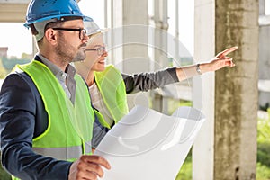 Young female architect pointing at something to her colleague at a construction site