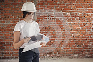 Young female architect with tablet checking blueprints against of building new modern house. Stylish happy woman engineer in hard