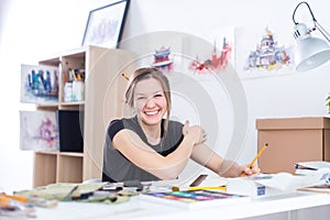 Young female artist drawing sketch using sketchbook with pencil at her workplace in studio. Side view portrait of