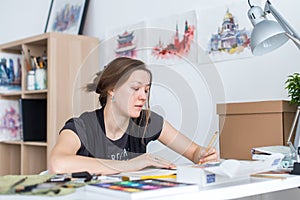 Young female artist drawing sketch using sketchbook with pencil at her workplace in studio. Side view portrait of