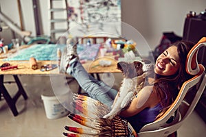 A young female artist is sitting in the chair with his dog and enjoying a break in her studio. Art, painting, studio