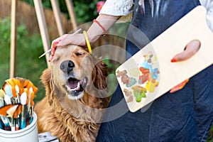 Young female artist working on her art canvas painting outdoors in her garden with golden retriever keeping her company.