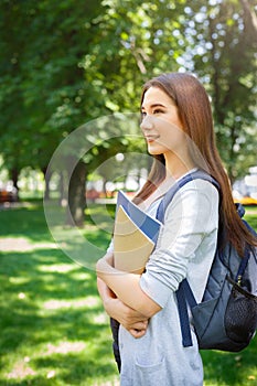 Young female asian IT student, with books and backpack. Staying in the park and smiling