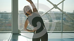 Young female athlete bending sidewards training alone in modern glass wall gym