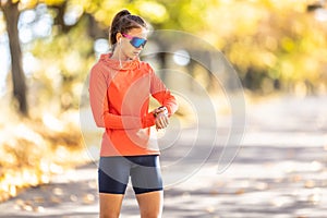 A young female athlete checks her running performance on a smart watch, listens to music through headphones and wears sports