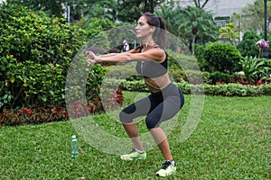 Young female athlete doing squat exercises outdoors in park. Fit girl working out her core and glutes with bodyweight. photo