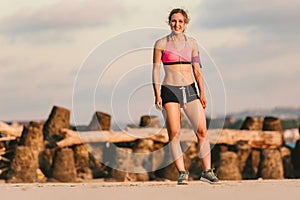 young female athlete in earphones with smartphone in running armband case standing on sandy