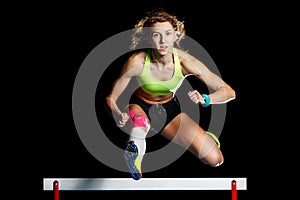 Young female athlete jumping over hurdle in sprint