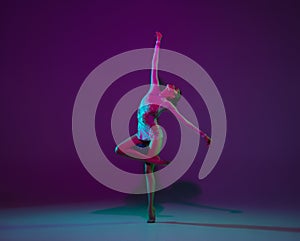 Young female athlete, rhythmic gymnastics artist on purple background with neon light. Beautiful girl practicing with