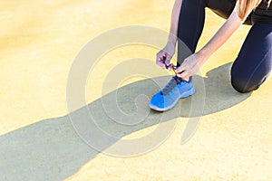 Young female athlete tying blue sports shoes and projecting shadow on yellow floor