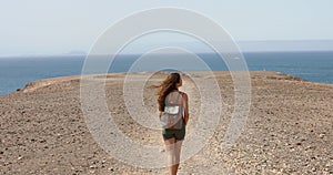 Young female backpacker enjoying ocean breeze and looking Fuerteventura Island in front of her. Hiker traveler girl walking.