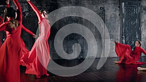 Young female ballet dancers are dancing con temporary dance in rehearsal in dark hall, red dresses are swaying