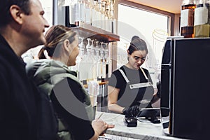 Young female barista takes order from her customers and selects coffee drinks on tablet