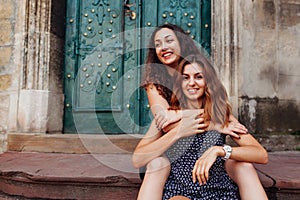 Young female best friends sitting on stairs and hugging. Happy girls laughing and having fun