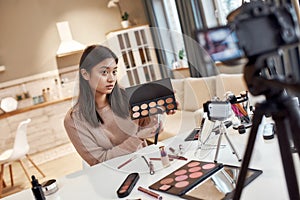 Young female blogger applying makeup, testing cosmetic products while recording a tutorial video for her beauty blog