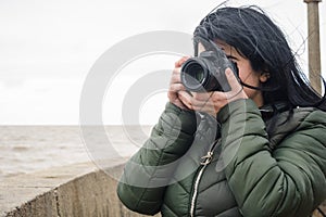 young female blogger content creator on a pier by the water taking photos with her digital camera