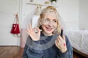 Young female blogger, content creator showing lipstick and okay hand sign, recommending beauty product for her audience