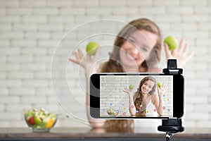 Young female blogger and vlogger and online influencer live streaming a cooking show on social media using a smartphone