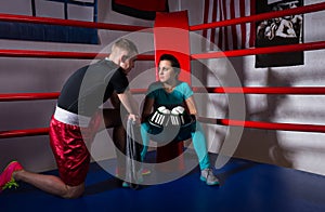 Young female boxer in boxing gloves after battle sitting next co