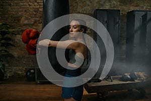 Young female boxer fighter hugging punching bag after intense workout