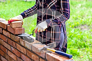 A young female bricklayer lays out cement mortar for laying bricks with a trowel on a brick wall.