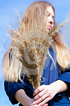 Young female with bunch of dried grass in hands. Long haired woman