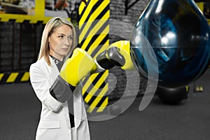 Young female businesswoman in a white suit hits a punching bag in the gym. The concept of office employee anger and