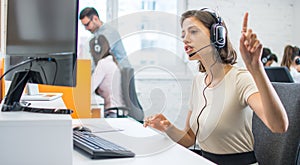 Young female call center operator with hands-free headset talking with client in office