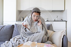 Young female calling doctor sitting on sofa with running nose