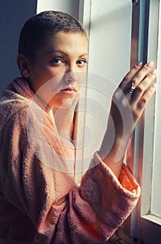 Young female cancer patient standing beside hospital window