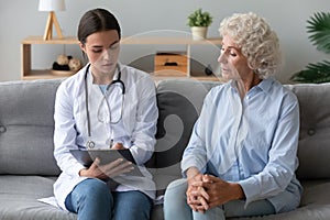 Young female caregiver listen writing health complaints of elderly woman photo