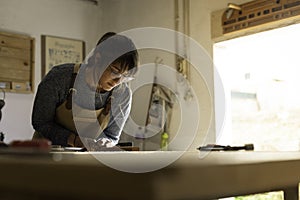 A young female carpenter working as wood designer in a small carpentry workshop. Young business woman handcrafting a piece of