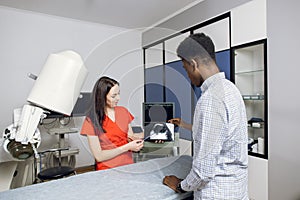 Young female caucasian doctor in modern clinic, holding tablet pc and showing to her male african patient ultrasound