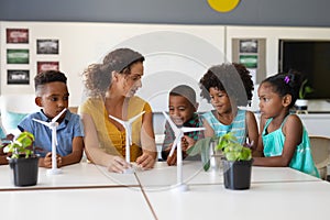 Young female caucasian teacher showing windmill model to african american elementary students